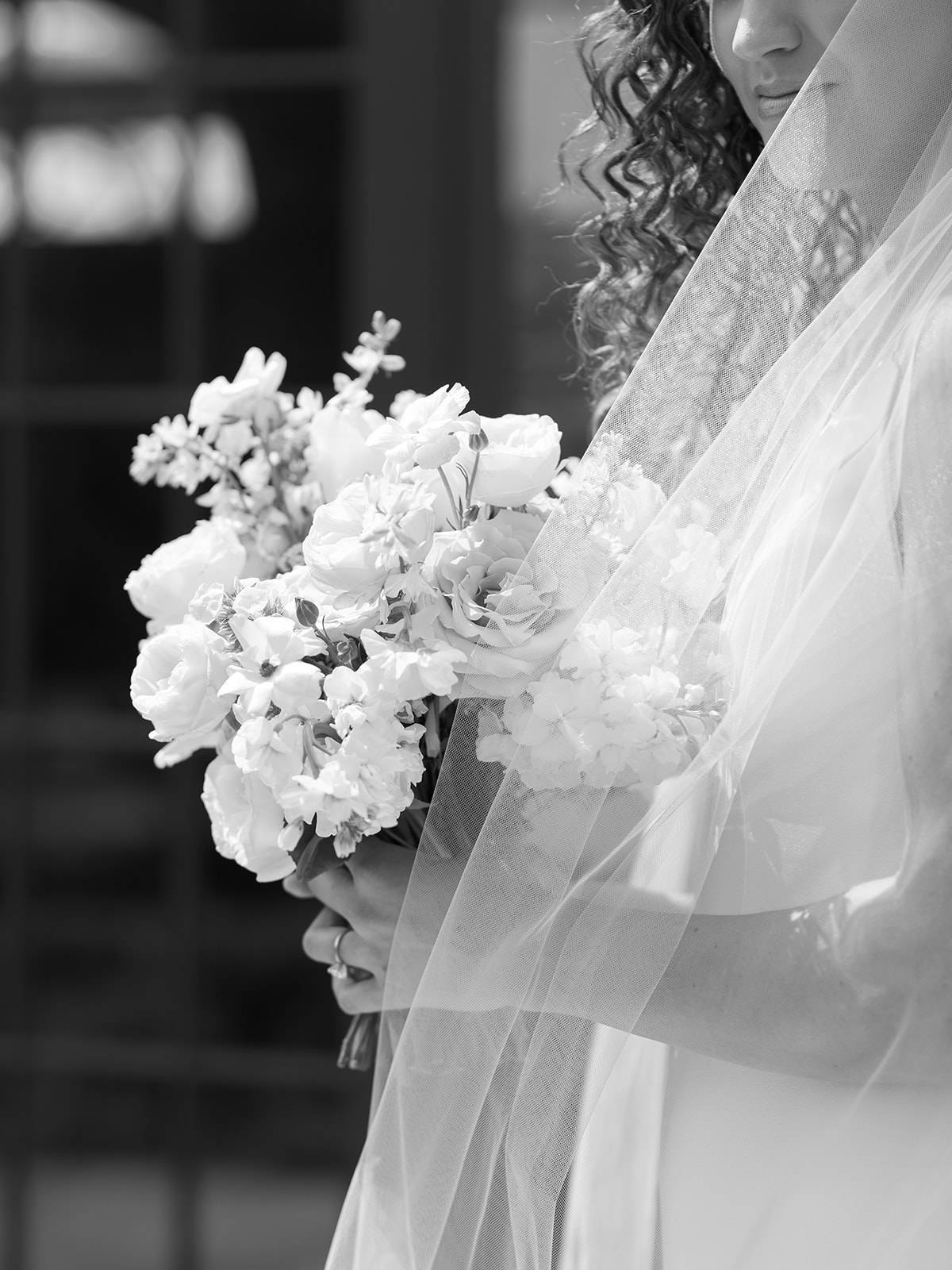 Black and white photo of a bride holding a bouquet with her veil flowing over the flowers and her shoulder.